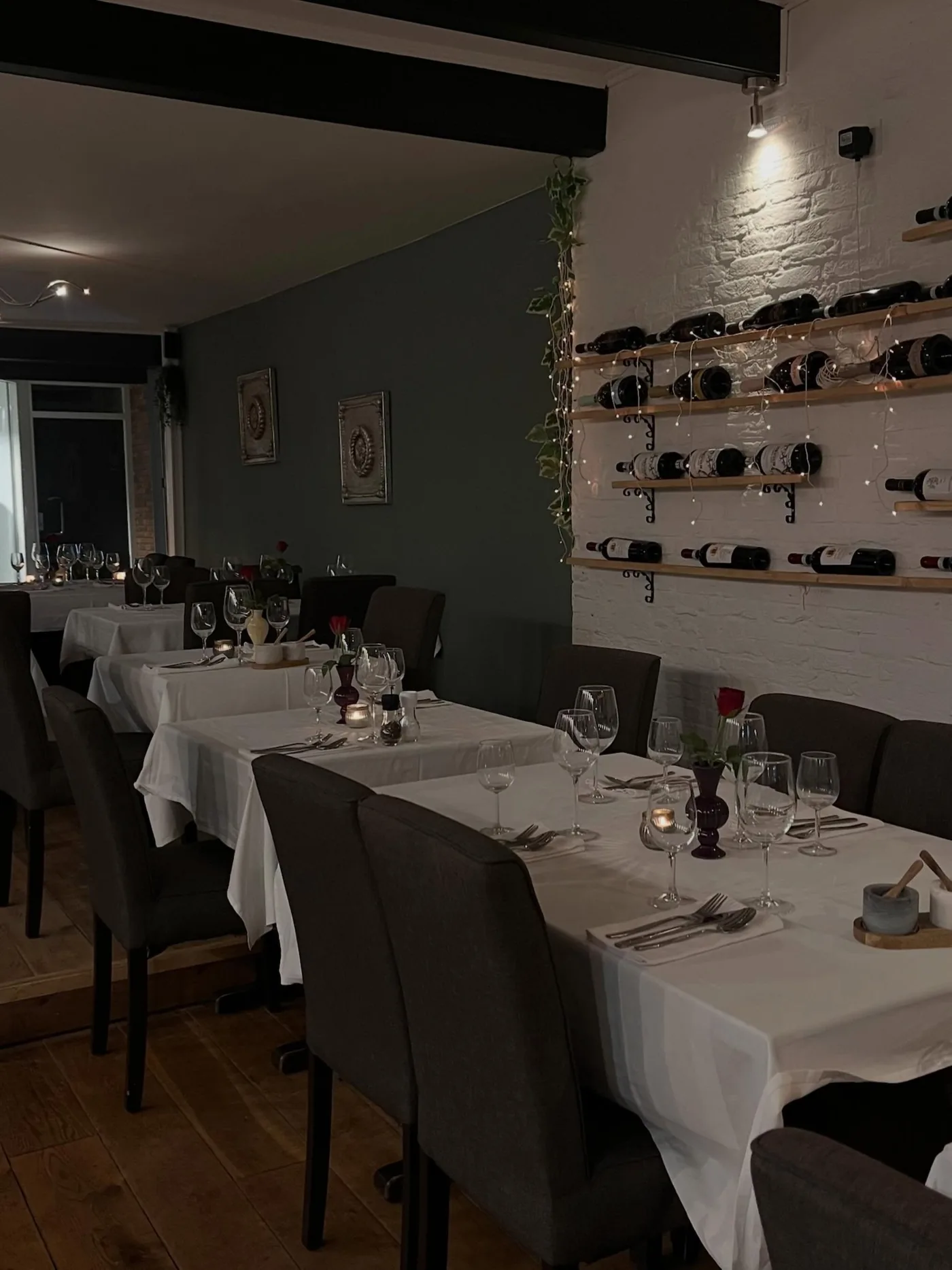 Het restaurant: lange tafels met witte kleden en de wand met wijnflessen